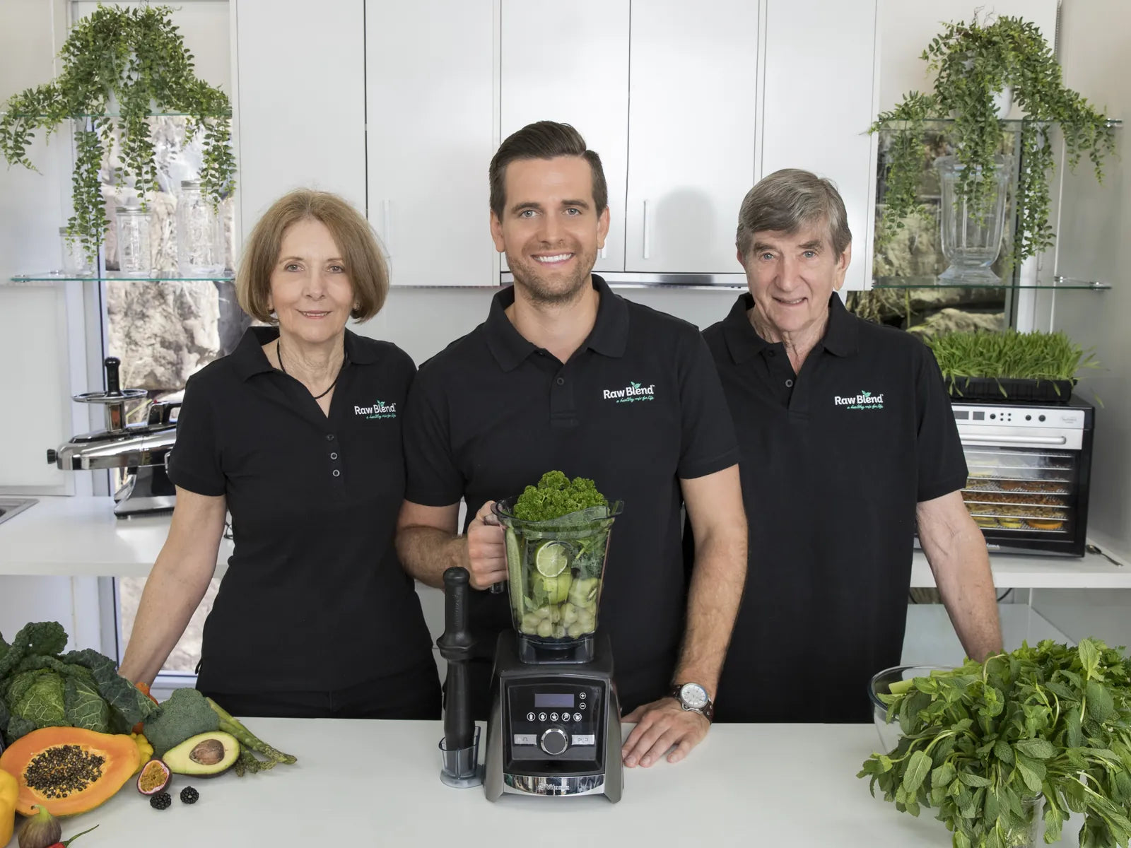 The Raw Blend family in their kitchen, standing behind a Vitamix and fresh produce