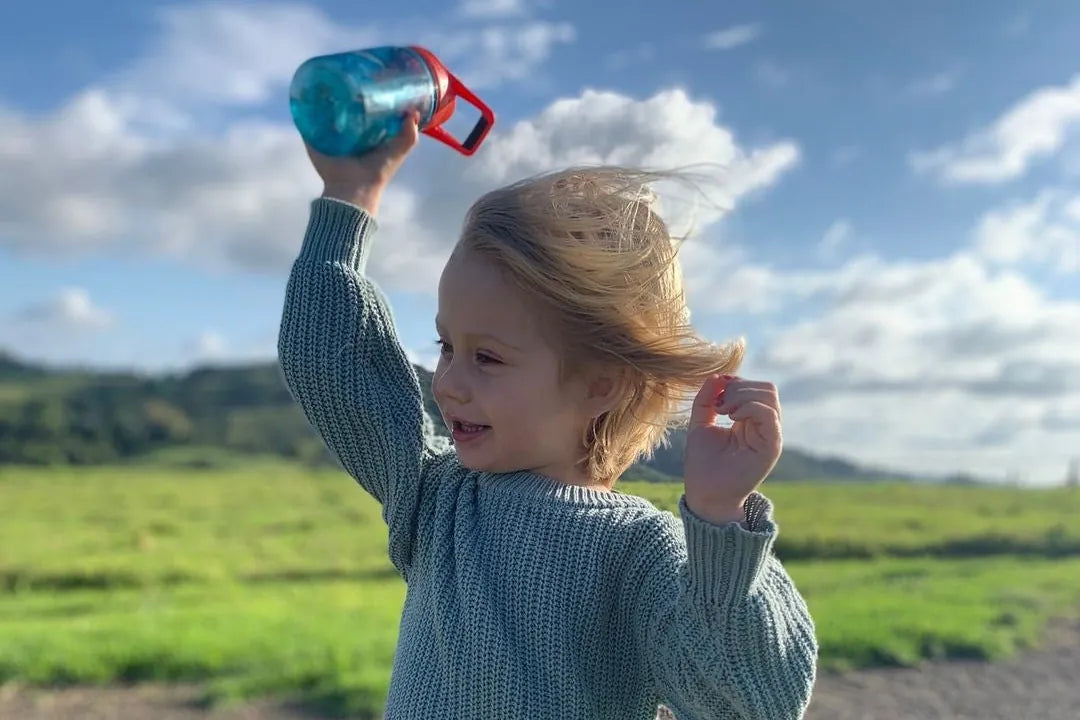 A child holding up an EcoVessel kids bottle in a green field