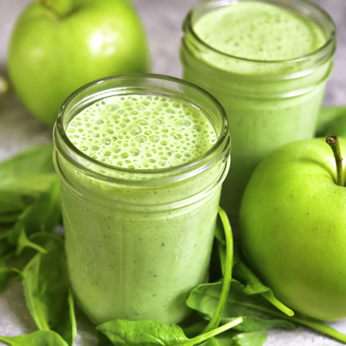 Two green smoothies in glass jars with fresh green apples and spinach leaves