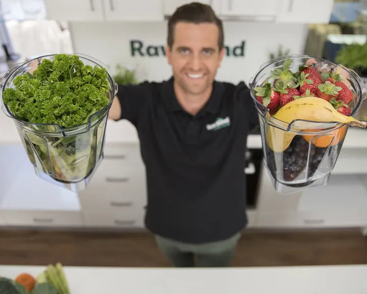 Tommy holding up a Vitamix jug of fresh greens and another of berries