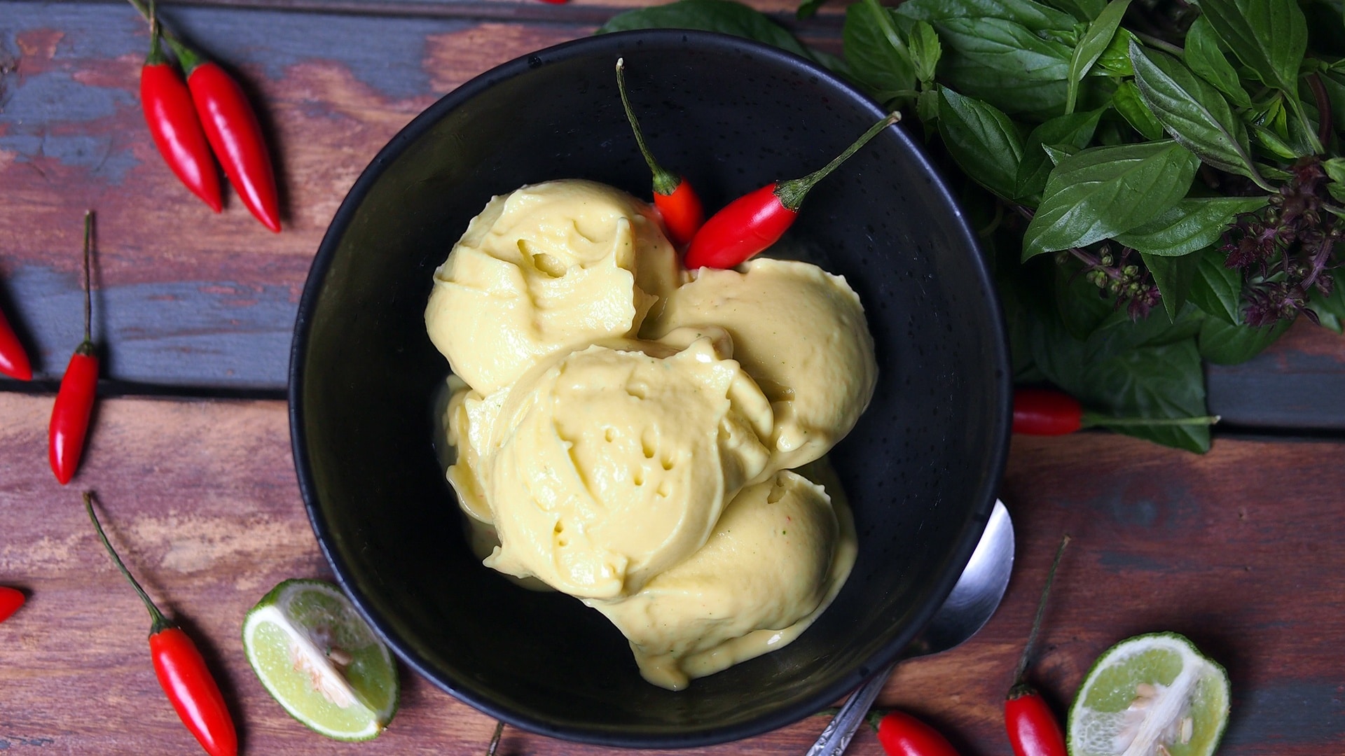 Photo of mango ice cream ina black bowl surrounded by chillies
